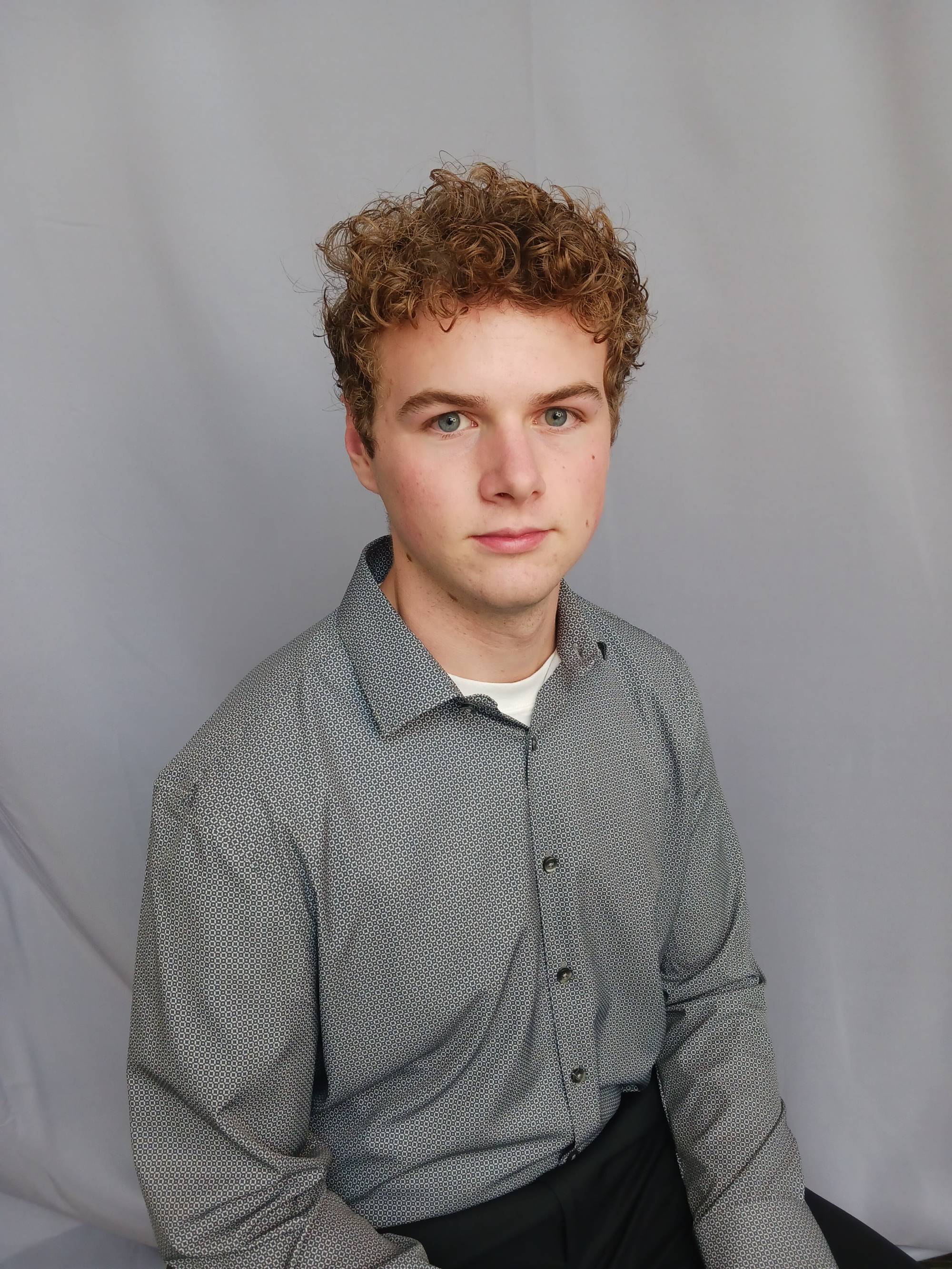 Young man with curly hair and a grey shirt looking at the camera